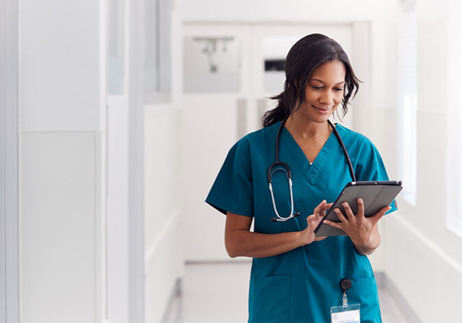 Female Doctor Wearing Scrubs In Hospital Corridor Using Digital Tablet